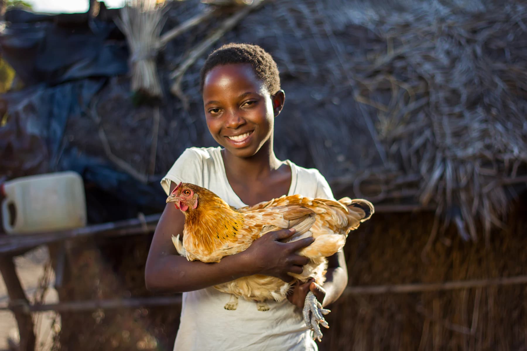A young poultry farmer smiles while holding one of her hens outside the coop